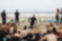A group of surfers on the beach listening to their instructor as he demonstrates how to pop up