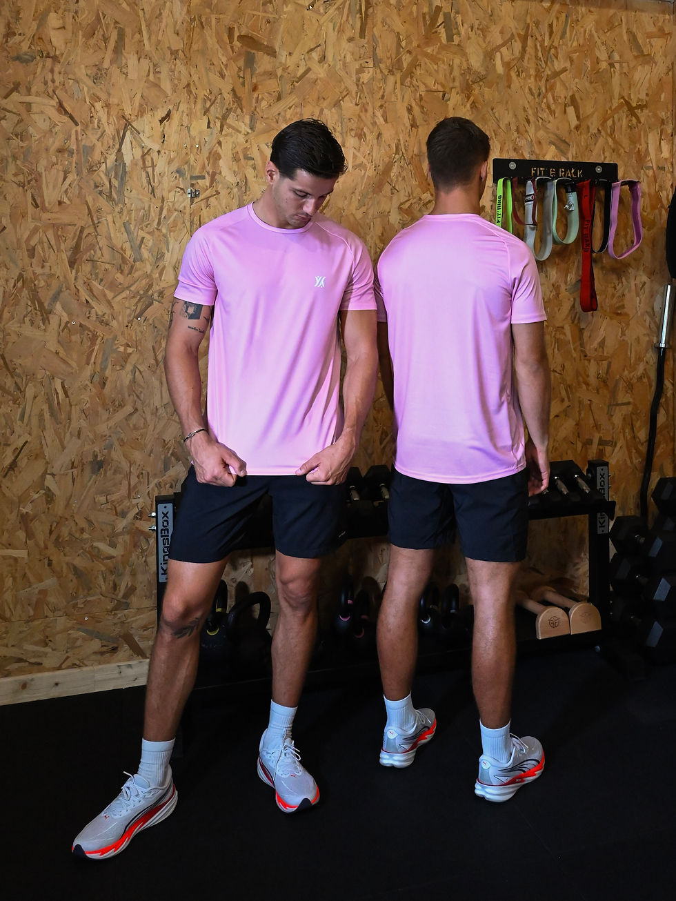 Duo d'hommes assortis portant le t-shirt de sport Essential rose en salle de sport, un homme de dos et l'autre de face
