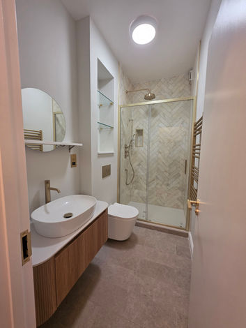 Bagno pulito e moderno con lavandino ovale, mobiletto in legno, WC e doccia in vetro.