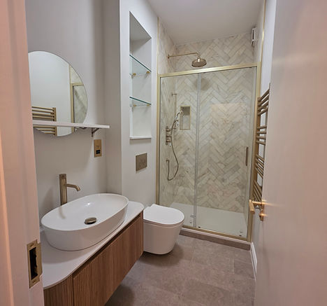Modern bathroom featuring wood vanity, white sink, toilet, glass shower, gold fixtures.