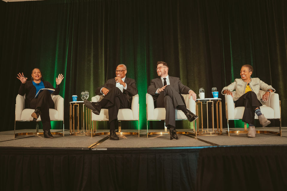 a 4 person panel of experts laughing on a big conference meeting stage
