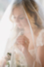 A bride in a white veil holds a bouquet, showcasing a sparkly ring. Soft lighting creates a dreamy and serene mood.