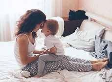 Mutter und Kind kuscheln lächelnd auf einem hellen Bett.