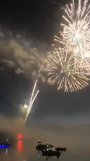 White fireworks explode in a black sky with boats on the reflective lake underneath. 