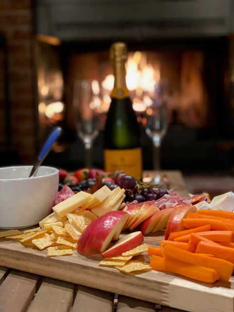 A roaring fireplace creates an appealing backdrop behind a charcuterie board and champagne bottle. 