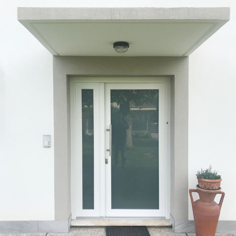 Portoncino d'ingresso moderno in PVC bianco con ampia vetrata e doppia anta, luce laterale fissa, maniglione in acciaio e pensilina superiore in cemento.