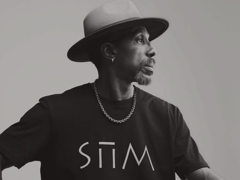 a black and white portrait of a black man wearing a black SIIM logo shirt and a hat