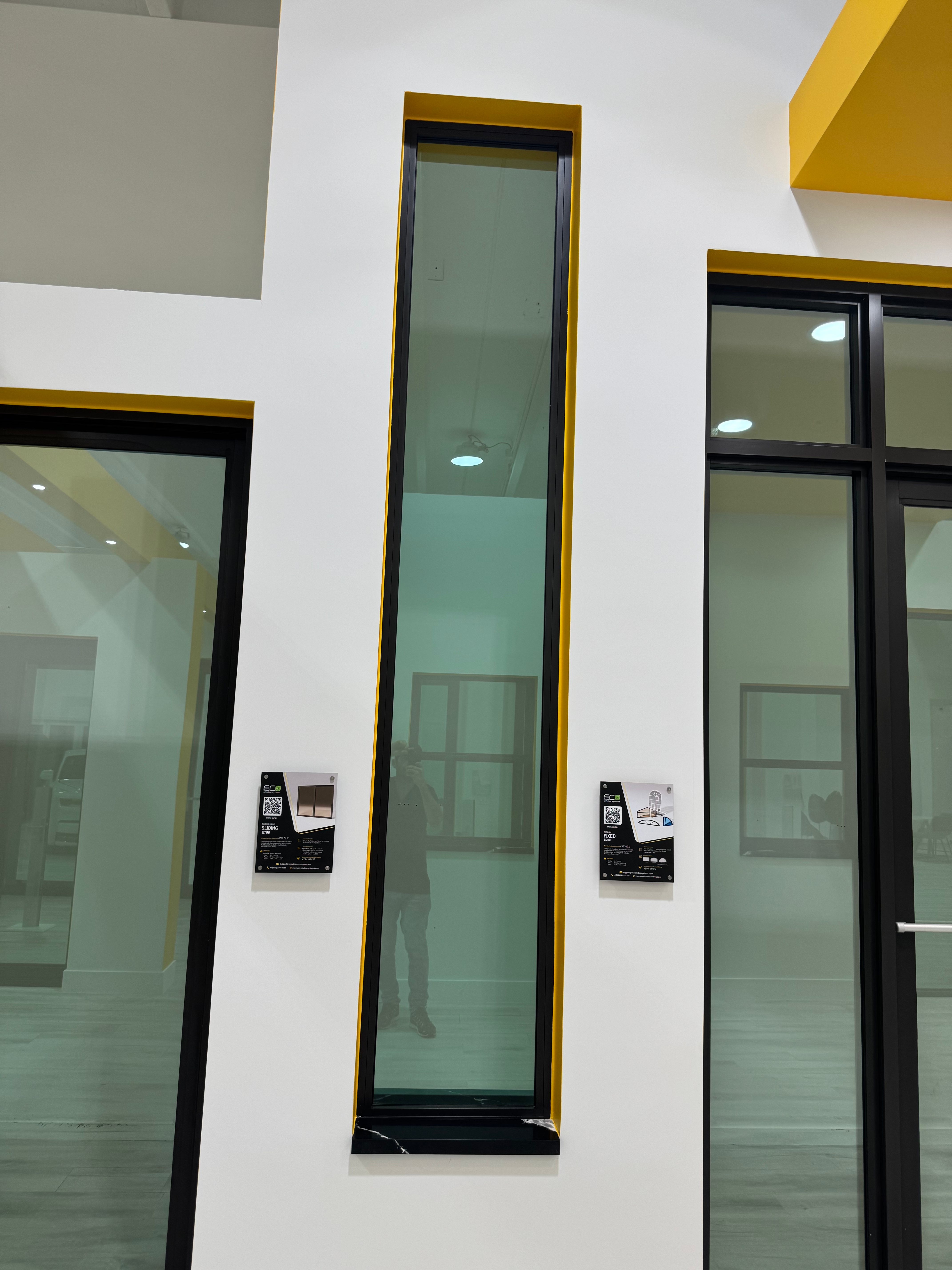 Tall black window frame, white walls, IMPACTWINDOWSWIN, display with QR codes on walls and doors