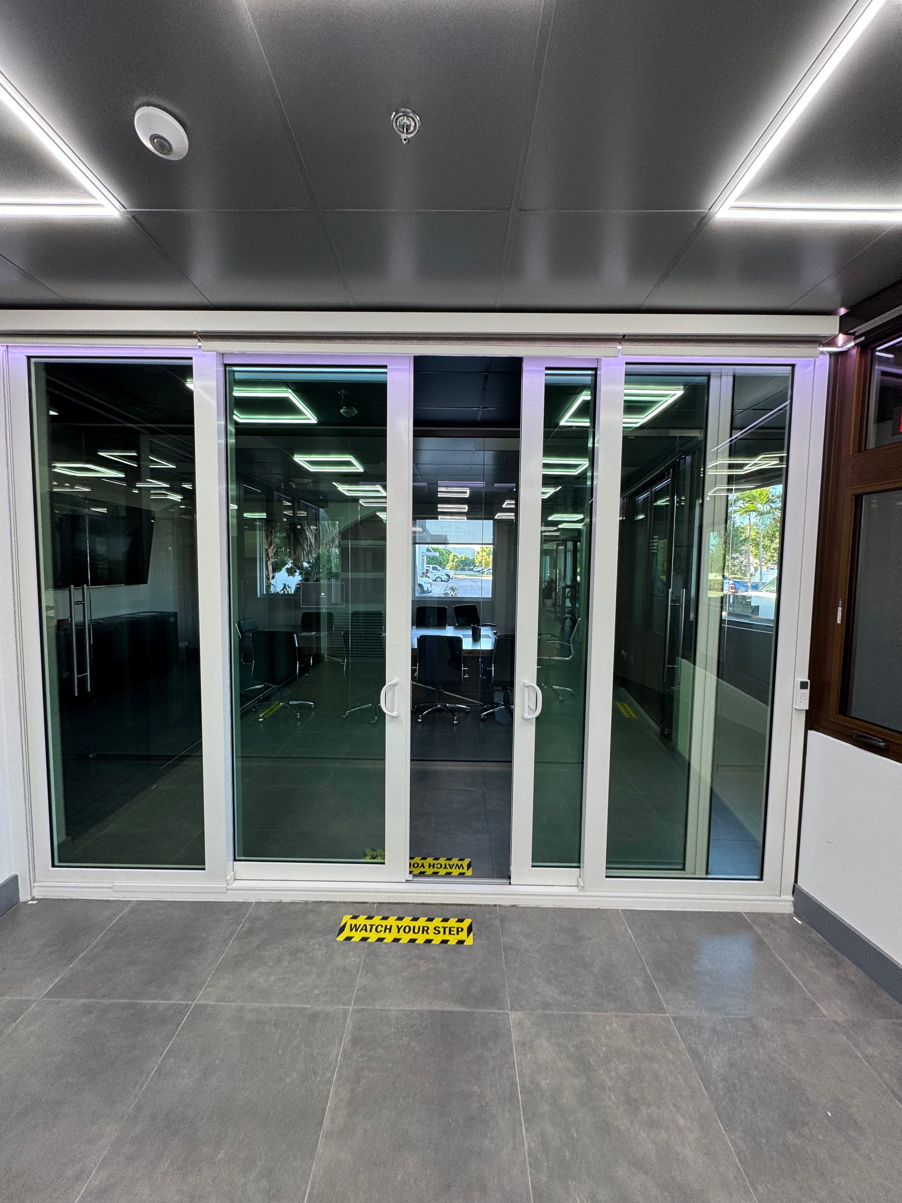 Glass sliding doors open to a conference room. Yellow caution tape on the floor.