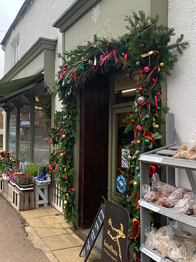 This is a side on photo of Perkins Florist. The doorway is decorated with a Christmas garland. Outside the shop window there are plants for sale.