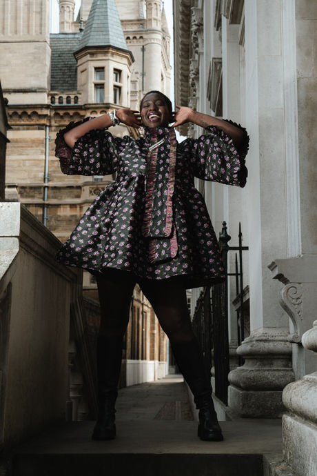 Black editorial model in a printed dress laughing on stone steps, a feminist photographer UK portrait