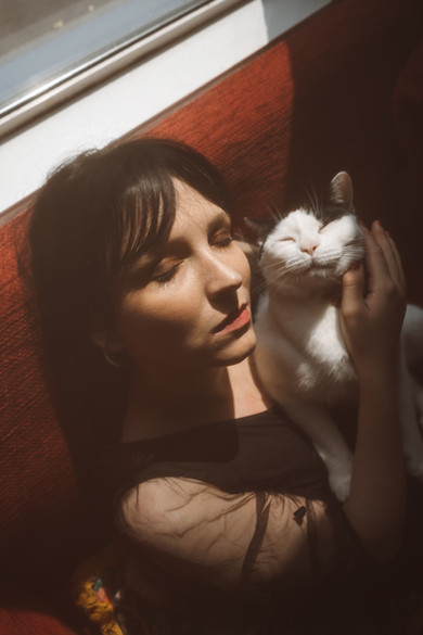 Woman with dark hair holding a white cat close to her face in warm indoor light