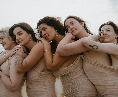 Group of women draped in sheer fabric leaning on each other on a beach during a body confidence group photoshoot in Brighton