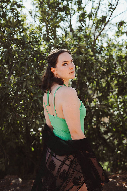 Woman in a green strappy top looking over her shoulder among sun-dappled foliage during a natural portrait photography session