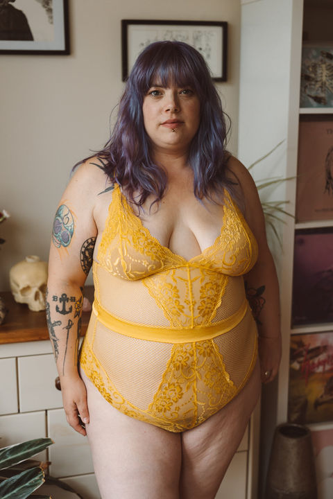 Plus size woman standing confidently in yellow lace lingerie during a body positive portrait session UK