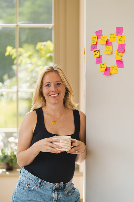 Woman standing by a wall decorated with pink and yellow Post-it notes shaped like a heart