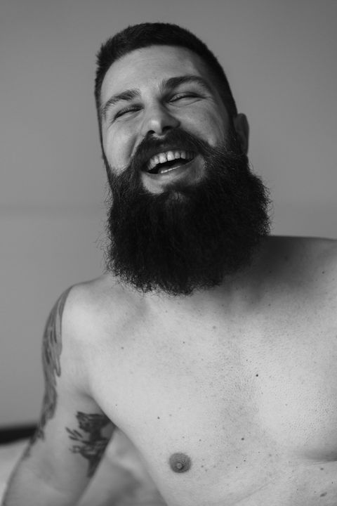 Black and white portrait of a laughing bearded man looking upward, shirtless