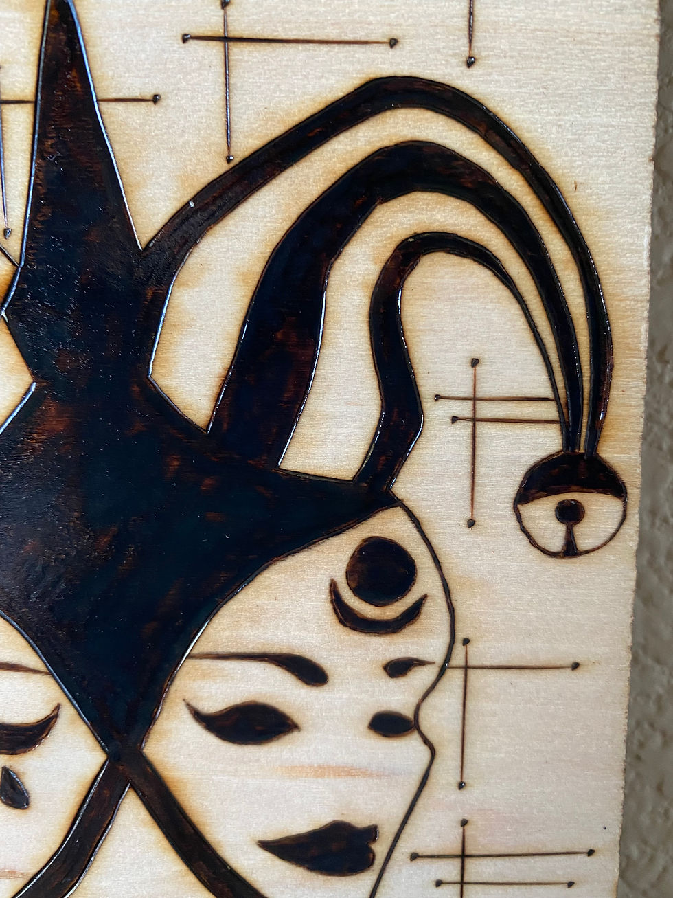 Thumbnail: Pyrography artwork depicting two faces with jester hats close up of the right side