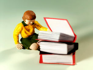 Small plastic toy girl in yellow jumper sat by pile of red books