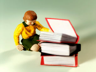 Small plastic toy girl in yellow jumper sat by pile of red books