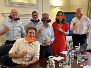 Five men and one woman in smart casual dress in a board room holding up cardboard employee ownership smiles