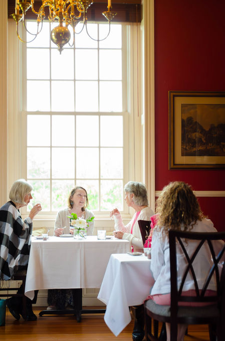 Four women sit around a table with a window in the background.