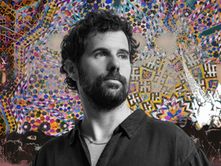 Nick Mulvey in black and white in front of a vibrant background, one image of which is from an album cover.