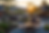 Outdoor dining with people at wooden tables, vibrant sunset, string lights, lush greenery, cozy atmosphere, and distant mountains.