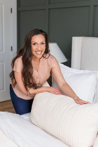A smiling woman fluffs a pillow on a nicely made bed - Personal Branding Photos NOVA