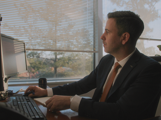 A man looking at two monitors on his desk in the evening.