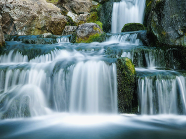 Cascading waterfall over moss-covered rocks, creating a serene and peaceful atmosphere. Water flows smoothly, surrounded by natural stone.
