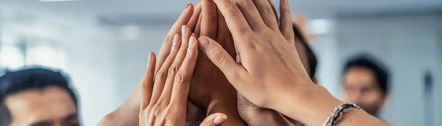 Close-up of colleagues joining their hands together in a high five or huddle, symbolizing teamwork and support.