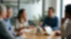 Diverse corporate team in a sunlit office having an engaged, safe discussion around a wooden table with a small plant and symbolic blocks.