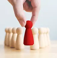 A hand lifting a single prominent red wooden figure out of a group of plain white figures, representing leadership and team care.