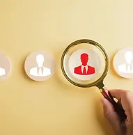 A hand holding a magnifying glass over a red professional icon among white ones, representing individual career health navigation.