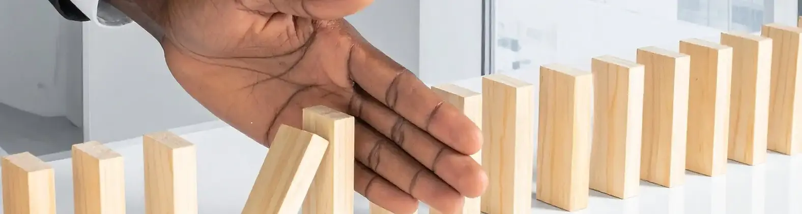 A hand stopping a row of falling wooden domino blocks, illustrating workplace resilience.