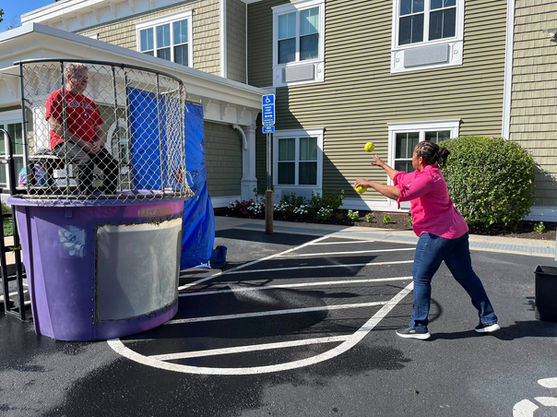 A woman throwing a ball at the target trigger of a purple outdoor dunk tank rental at a community event.
