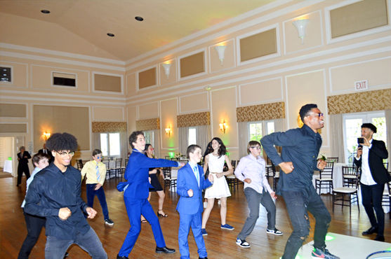 An interactive DJ motivator leading kids and teens in group dancing on a ballroom dance floor during a Jewish event.