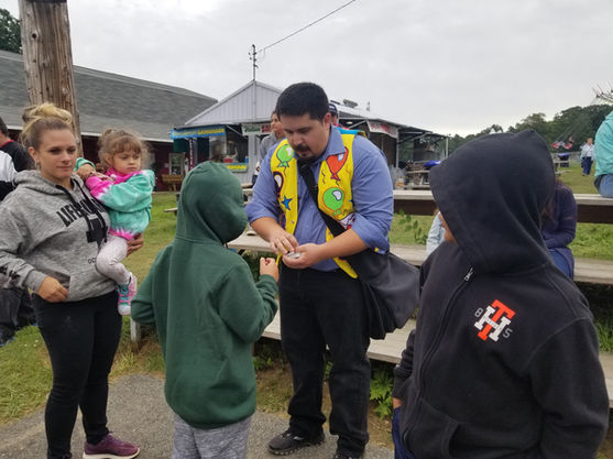 A street magician performing sleight-of-hand card tricks up close for children and families at an outdoor festival.