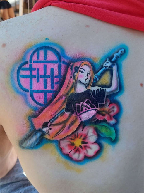 A vibrant temporary airbrush body tattoo featuring a stylized character and floral elements on a student's skin at a homecoming event.