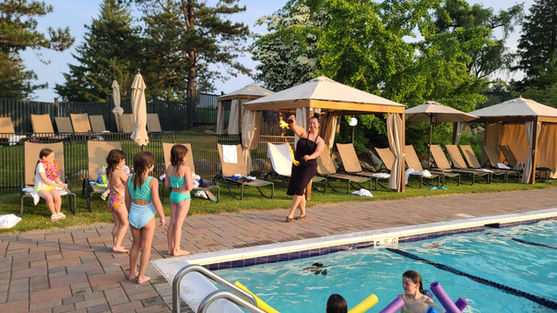 A fire and hula dancer performing with flaming props near an outdoor pool while children watch.