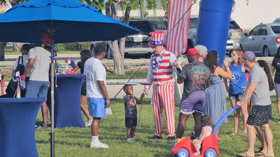 An Uncle Sam performer teaching a young boy how to spin plates at an outdoor patriotic festival.