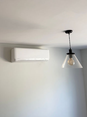 White mini-split AC unit mounted on wall beside a pendant light fixture