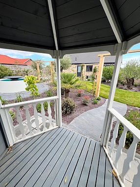 View of a landscaped garden and lawn seen through a wooden porch or veranda frame.