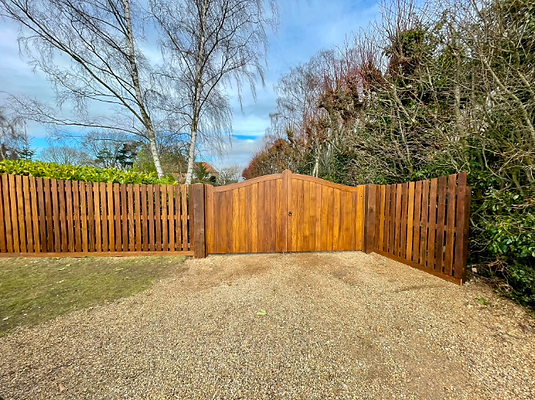 Tall wooden privacy gate and matching fence enclosing a gravel driveway area