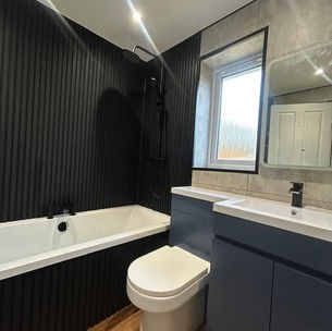 A modern bathroom renovation featuring black fluted wall panels behind a white bathtub and