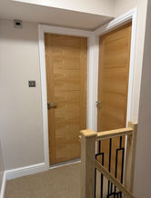 Hallway landing featuring contemporary light oak doors, white architraves, and wooden stair handrail