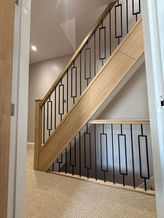 Staircase landing balustrade with light oak timber handrail and modern black metal geometric spindles