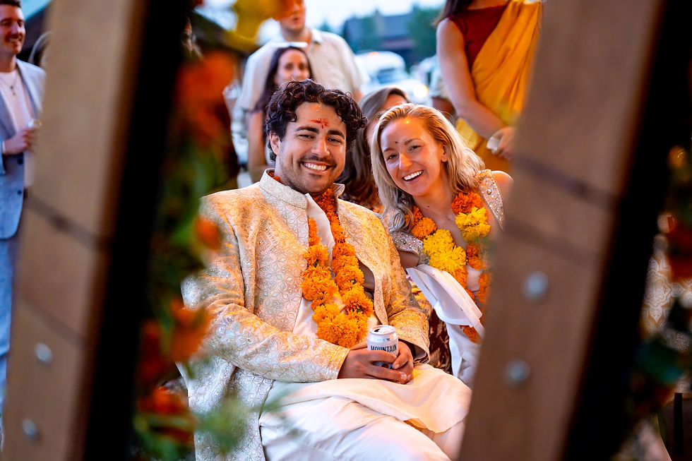 Bride and groom smiling at their sangeet at Estes Park Marina, wearing marigold garlands with blurred guests in the background