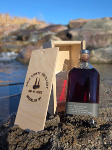 A picture of the King's County 10 year hazmat black label distillery release bourbon with wooden box in sand. Better than any Buffalo Trace